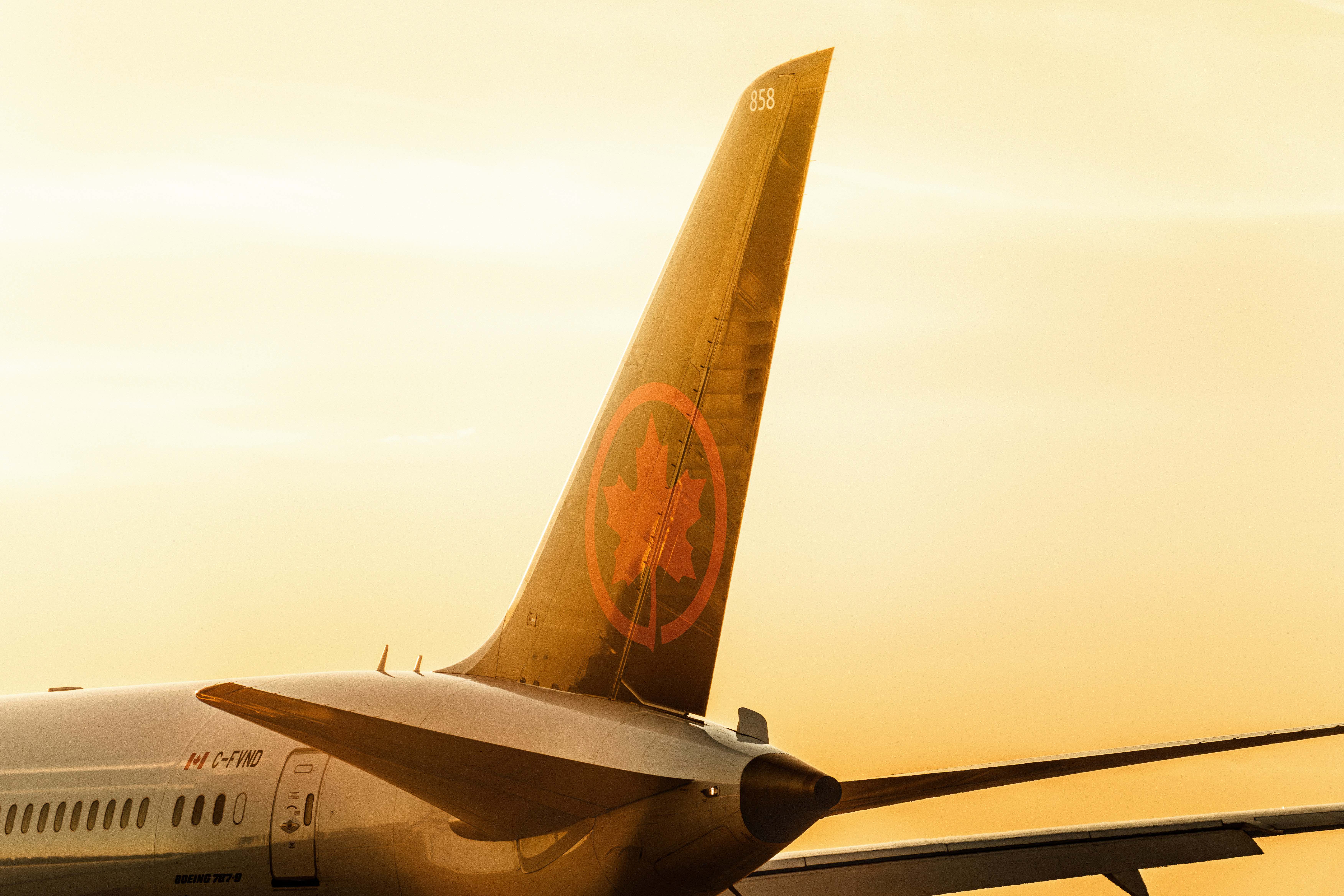 An Air Canada aircraft tail with the maple-leaf logo glowing in golden sunset light