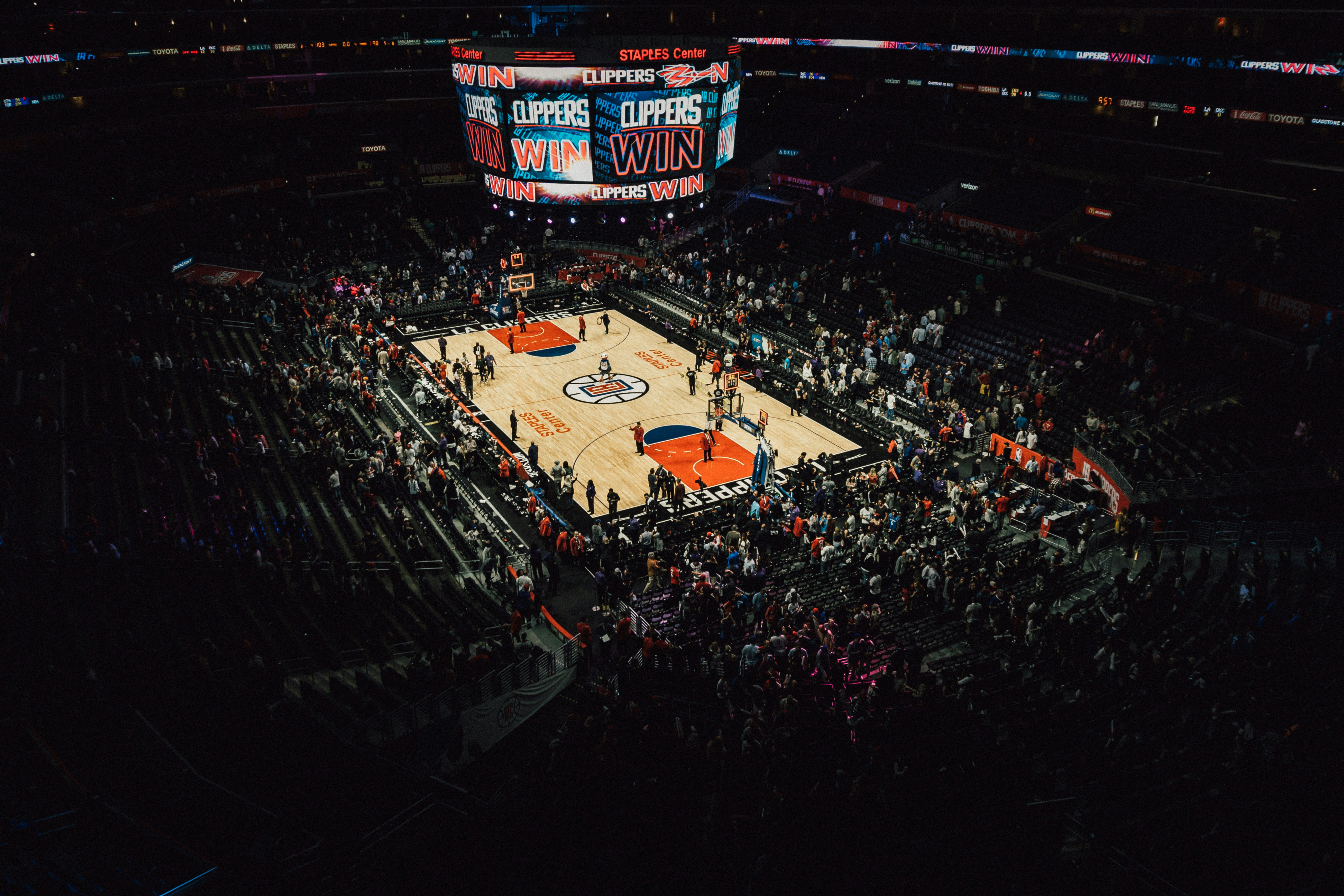 A professional basketball arena viewed from high in the stands, the lit court surrounded by crowds beneath a bright scoreboard