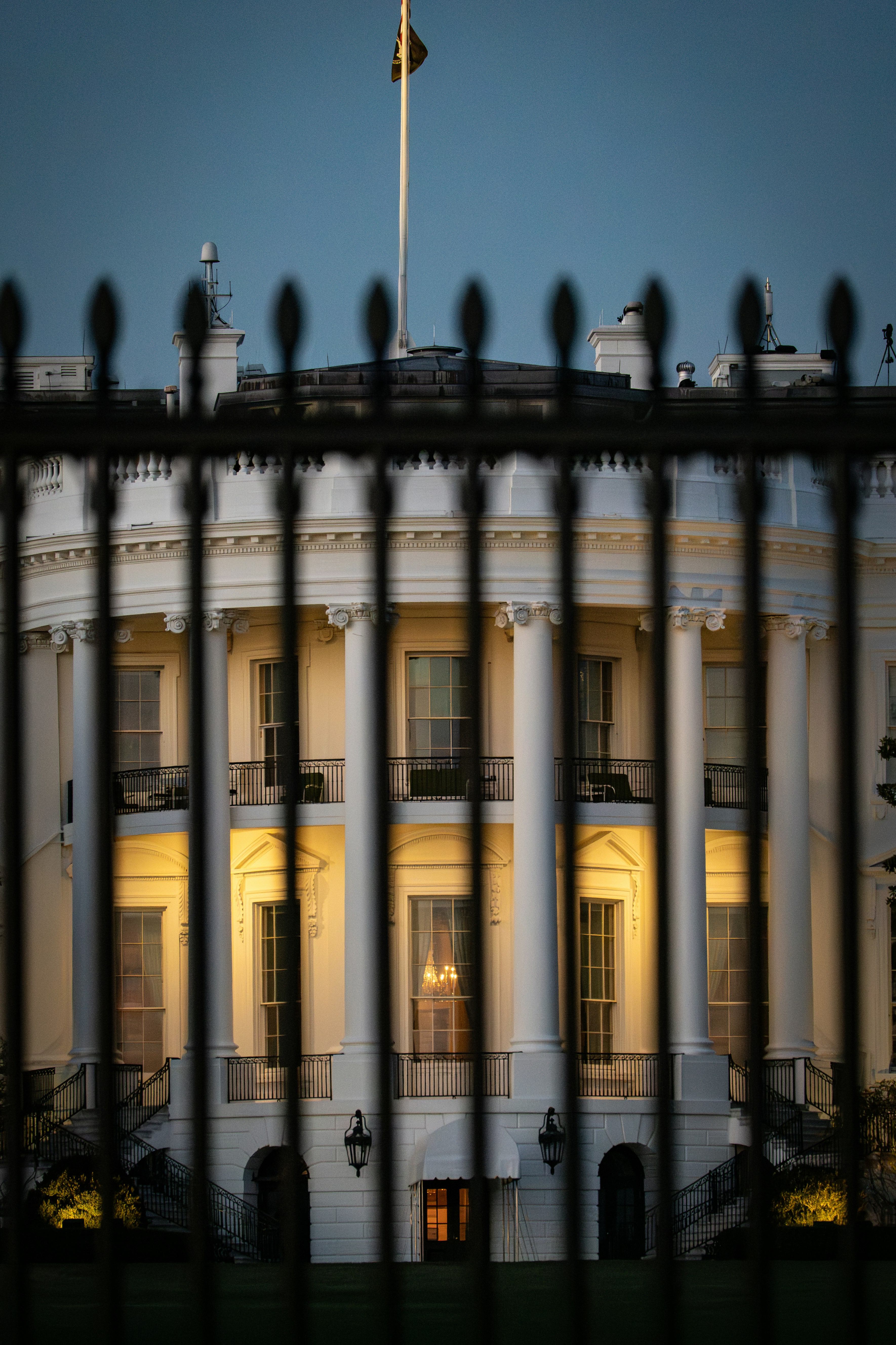 The White House illuminated at dusk, viewed through the iron fence on Pennsylvania Avenue