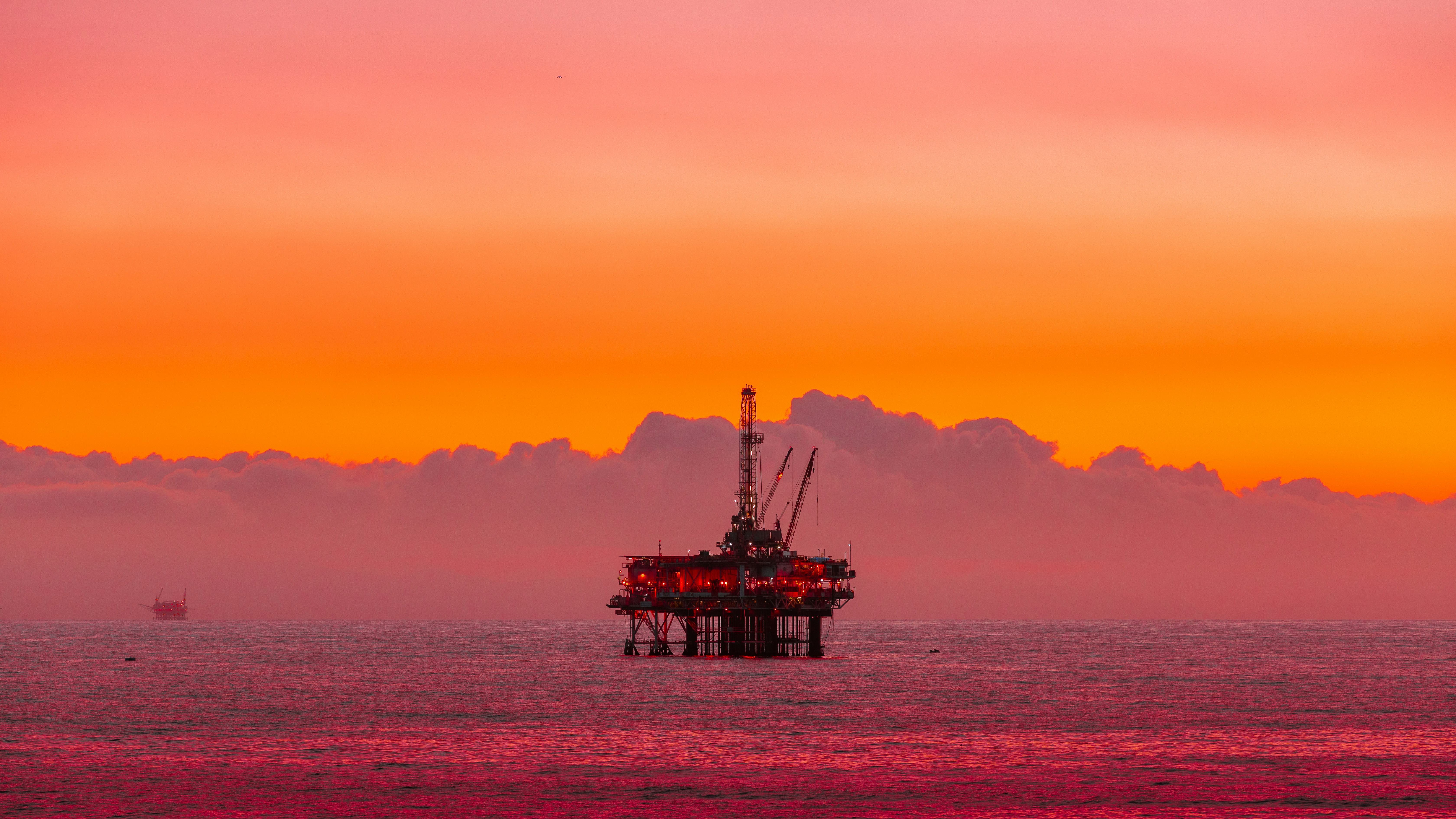 Offshore oil rig at sunset with dramatic orange sky and calm ocean