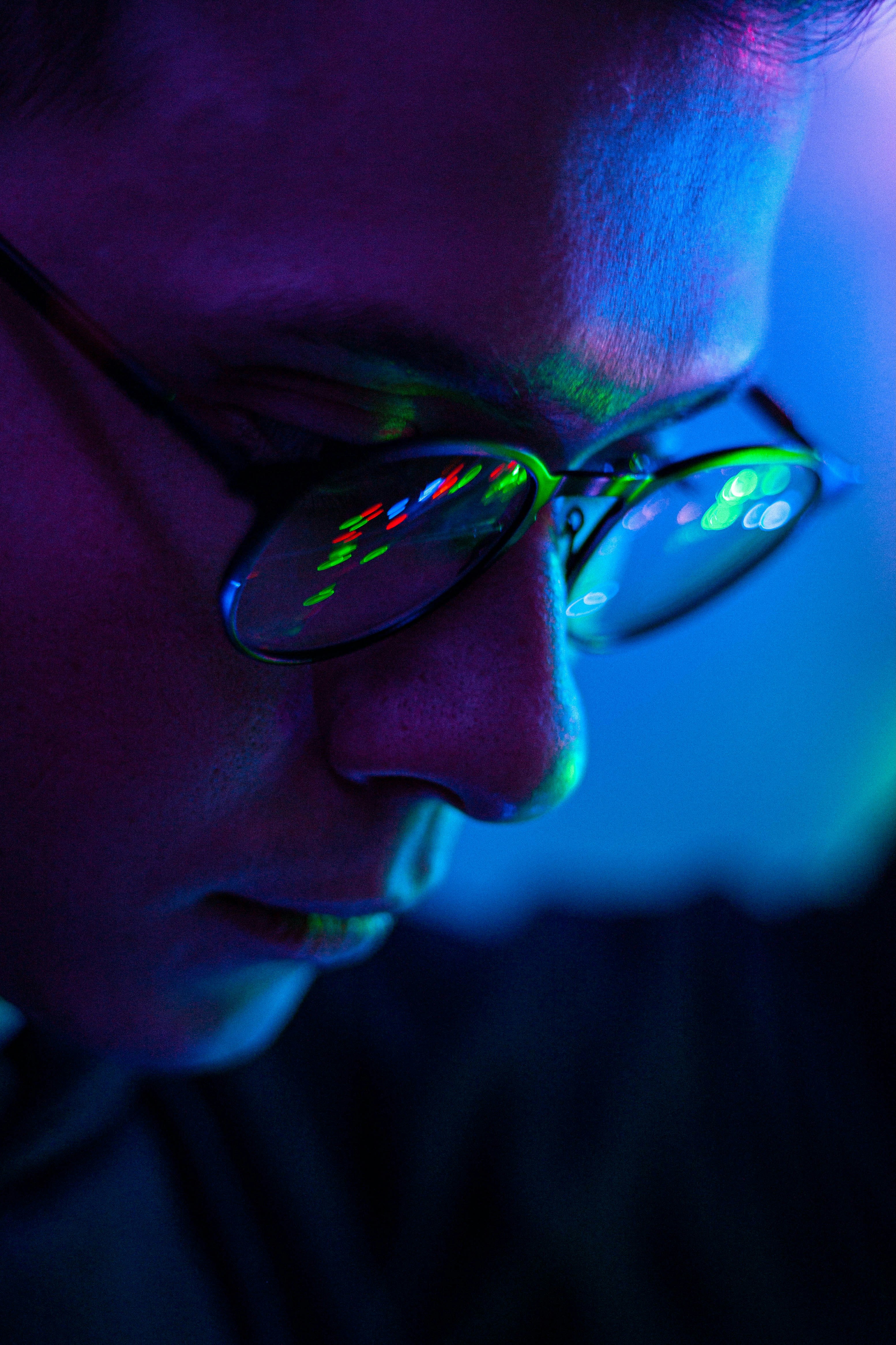 Close-up of a face illuminated by screen light with digital reflections in glasses